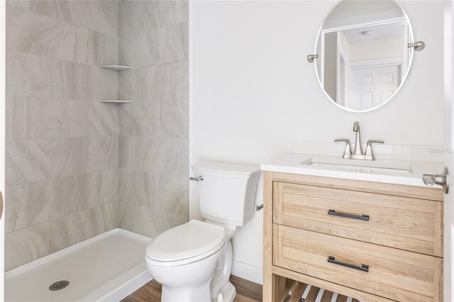 bathroom featuring a tile shower, vanity, toilet, and wood-type flooring