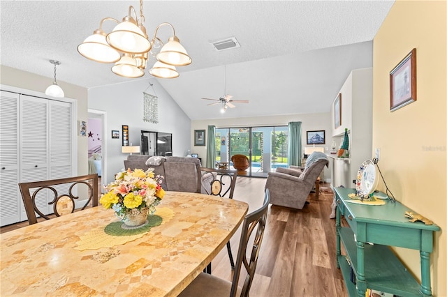 dining space with hardwood / wood-style floors, ceiling fan with notable chandelier, a textured ceiling, and vaulted ceiling