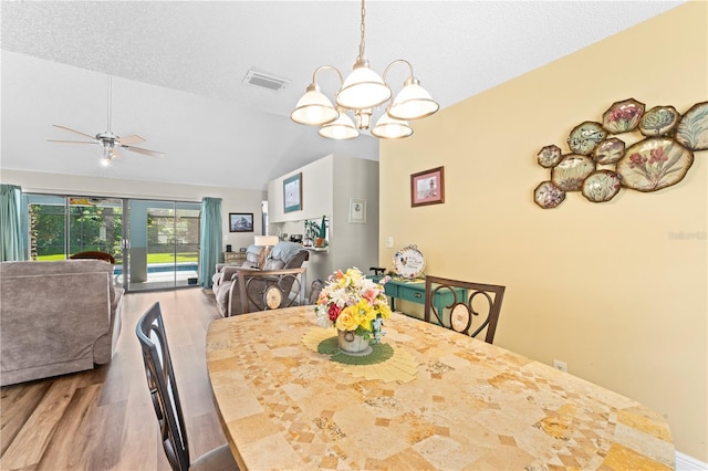 dining space featuring a textured ceiling, ceiling fan with notable chandelier, lofted ceiling, and wood-type flooring