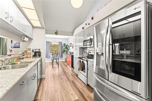 kitchen with white cabinetry, sink, stainless steel appliances, light hardwood / wood-style flooring, and pendant lighting