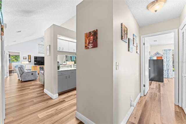 hall featuring light wood-type flooring, lofted ceiling, and a textured ceiling