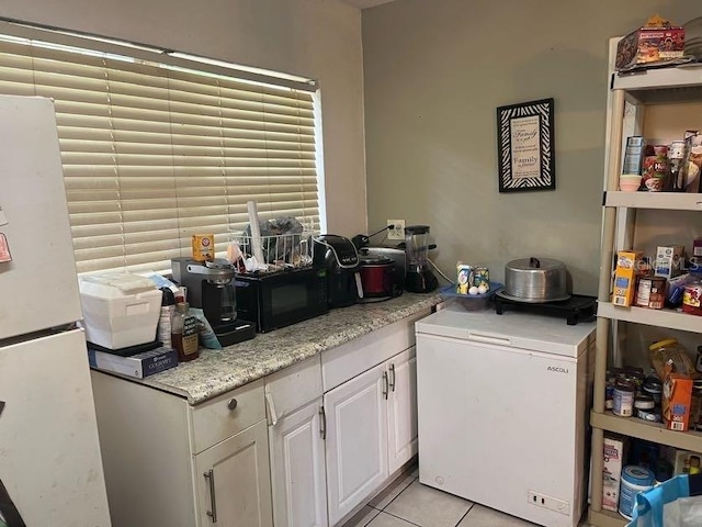 interior space with white cabinets, white fridge, light tile patterned floors, light stone countertops, and refrigerator