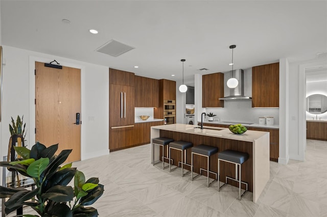 kitchen featuring sink, wall chimney range hood, a breakfast bar, a center island with sink, and decorative light fixtures