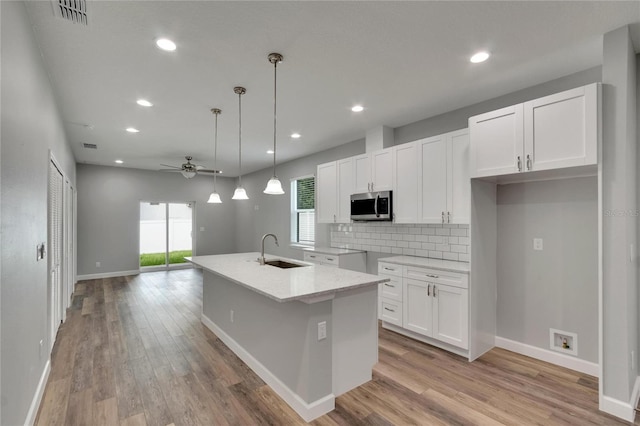 kitchen featuring ceiling fan, white cabinets, pendant lighting, sink, and a center island with sink