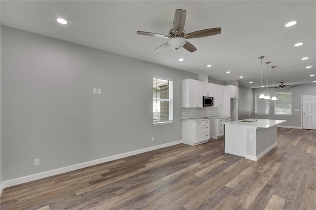 kitchen featuring ceiling fan, white cabinets, an island with sink, and decorative light fixtures