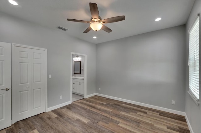 unfurnished bedroom featuring a closet, hardwood / wood-style flooring, sink, ensuite bathroom, and ceiling fan