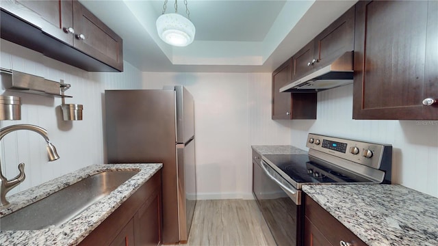 kitchen with appliances with stainless steel finishes, light stone countertops, light wood-type flooring, a tray ceiling, and sink