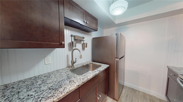 kitchen with stainless steel fridge, sink, dark brown cabinets, light stone countertops, and light hardwood / wood-style floors