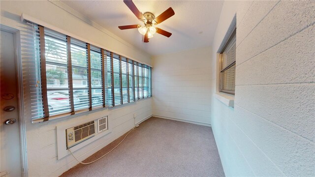 carpeted empty room with a wealth of natural light, a wall unit AC, and ceiling fan