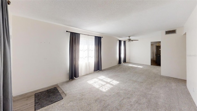 empty room featuring ceiling fan, a textured ceiling, and light carpet