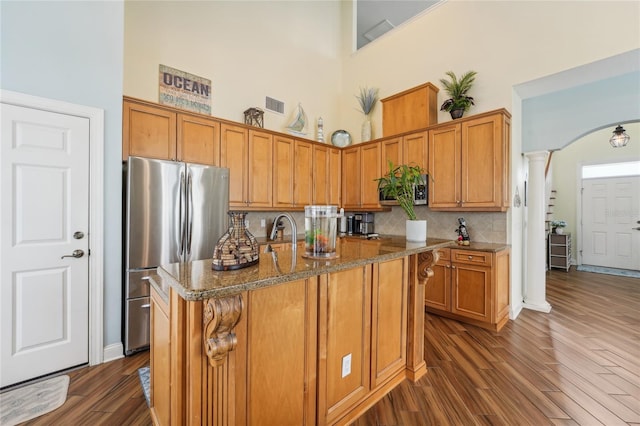 kitchen featuring a towering ceiling, a center island with sink, dark hardwood / wood-style floors, and stainless steel fridge