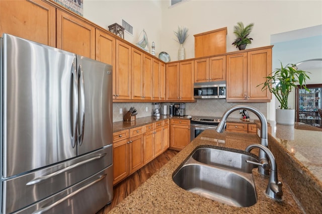 kitchen with tasteful backsplash, stainless steel appliances, stone counters, hardwood / wood-style floors, and sink