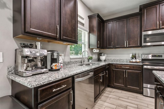 kitchen with appliances with stainless steel finishes, dark brown cabinets, sink, and light hardwood / wood-style flooring