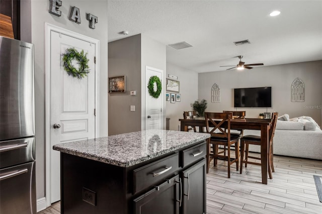 kitchen with ceiling fan, stainless steel refrigerator, a center island, light stone countertops, and light hardwood / wood-style floors