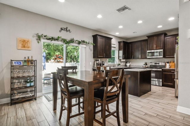 kitchen with dark brown cabinetry, sink, light hardwood / wood-style flooring, stainless steel appliances, and a center island