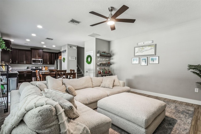 living room with ceiling fan, a textured ceiling, and dark wood-type flooring