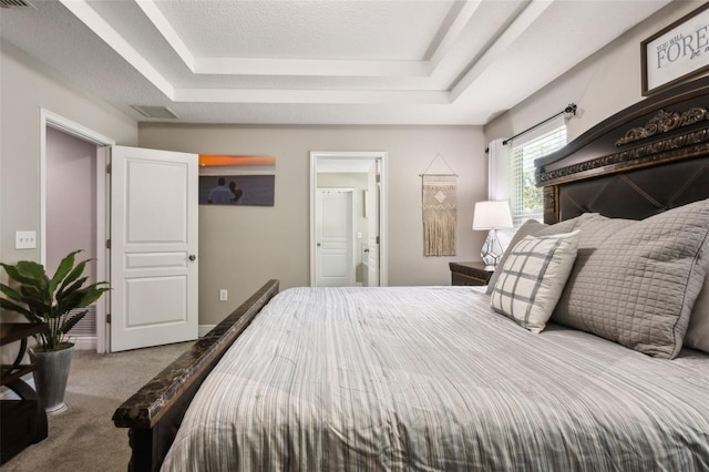 carpeted bedroom with a textured ceiling, a tray ceiling, and ensuite bathroom