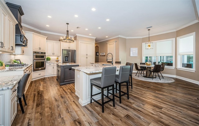 kitchen featuring a kitchen island with sink, dark wood-type flooring, stainless steel appliances, and decorative light fixtures