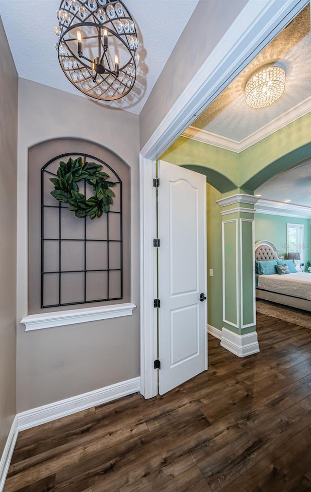 entrance foyer featuring crown molding, decorative columns, an inviting chandelier, and dark wood-type flooring