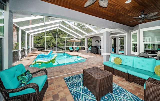 view of swimming pool featuring an outdoor hangout area, a patio area, glass enclosure, ceiling fan, and grilling area