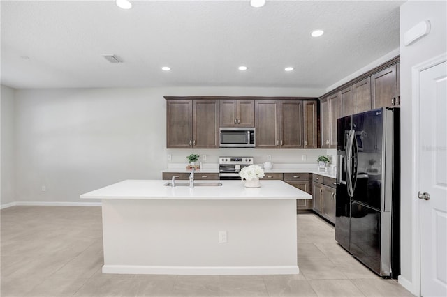 kitchen featuring dark brown cabinetry, appliances with stainless steel finishes, a kitchen island with sink, and sink