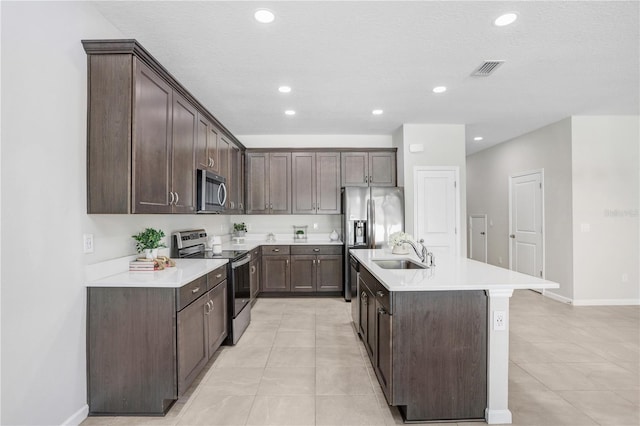 kitchen with an island with sink, appliances with stainless steel finishes, and dark brown cabinetry