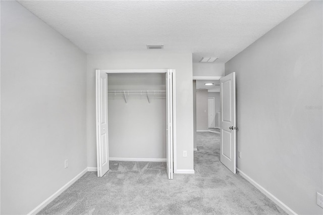 unfurnished bedroom with a closet, light colored carpet, and a textured ceiling