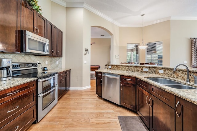 kitchen with light wood-type flooring, sink, stainless steel appliances, light stone countertops, and crown molding