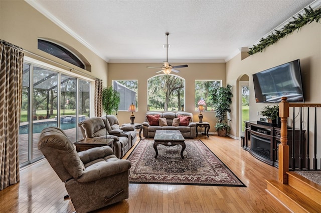 living room with a fireplace, a textured ceiling, wood-type flooring, crown molding, and ceiling fan