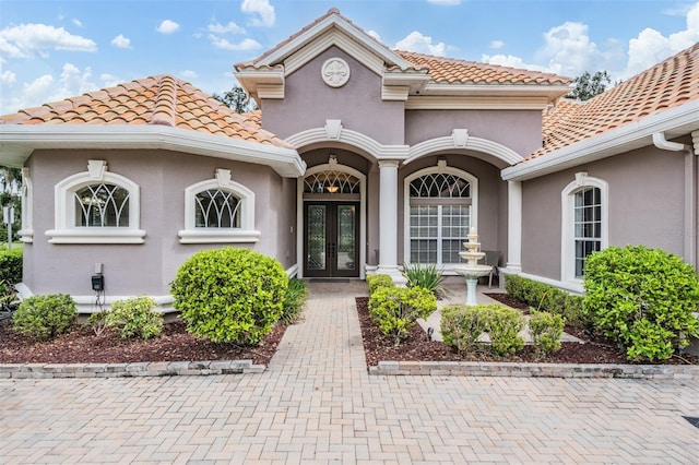 view of exterior entry with a tile roof, stucco siding, and french doors