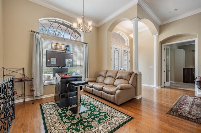 living room featuring wood-type flooring, ornamental molding, an inviting chandelier, and ornate columns