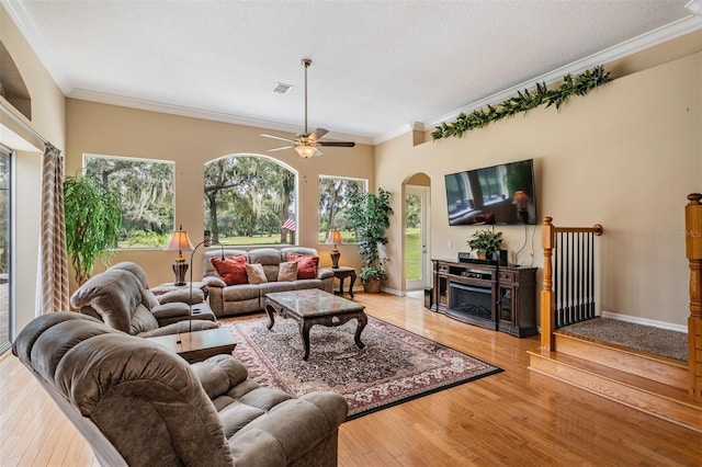 living room featuring ceiling fan, light wood-type flooring, crown molding, and a fireplace