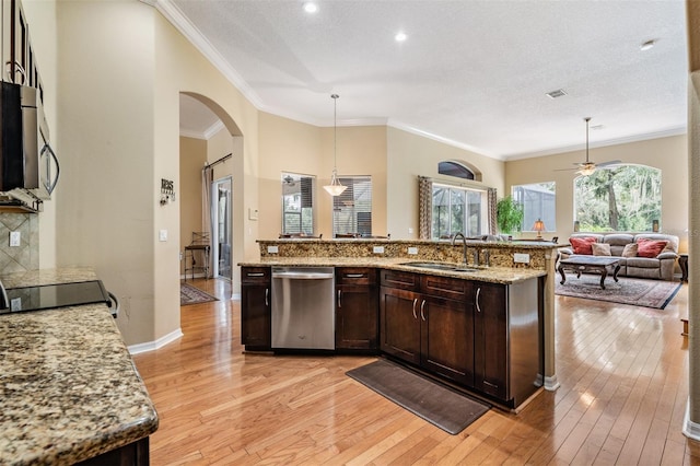 kitchen with stainless steel appliances, a sink, arched walkways, light wood finished floors, and dark brown cabinetry