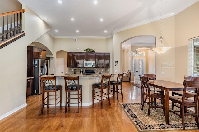 kitchen featuring hanging light fixtures, light hardwood / wood-style flooring, stainless steel appliances, dark brown cabinetry, and ornamental molding