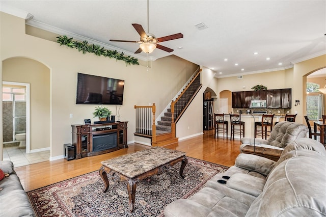 living area featuring crown molding, light wood-type flooring, visible vents, arched walkways, and ceiling fan