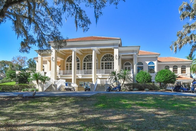 view of front of house featuring stairway, stucco siding, a tiled roof, a porch, and a yard