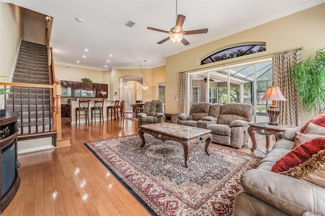 living room featuring light wood-type flooring, ornamental molding, arched walkways, visible vents, and ceiling fan