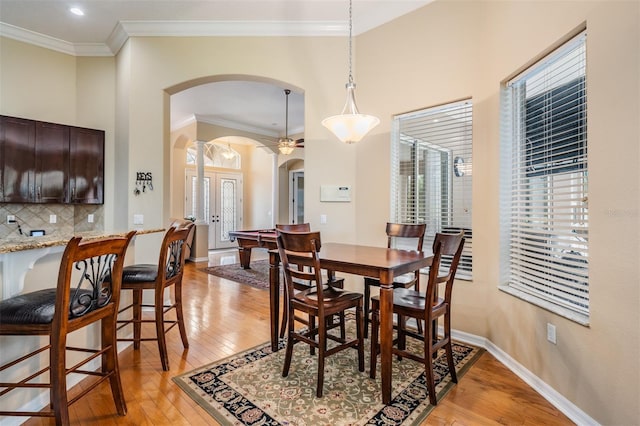 dining area with ornamental molding, arched walkways, baseboards, and light wood-style floors