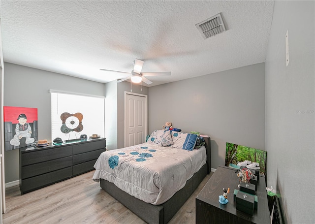 bedroom with ceiling fan, a textured ceiling, light hardwood / wood-style flooring, and a closet