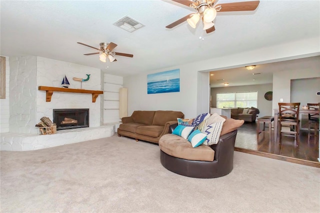 living room with carpet, ceiling fan, and a stone fireplace