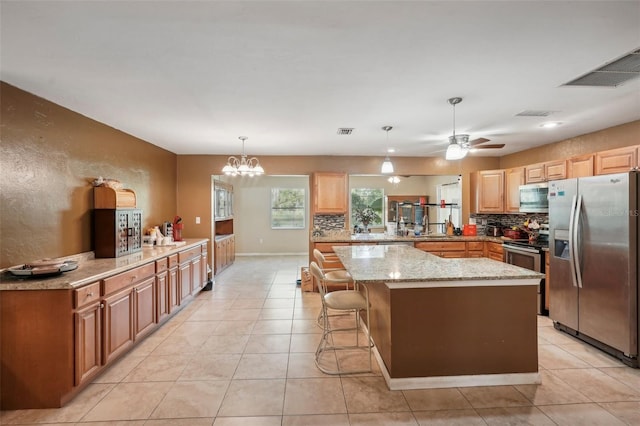 kitchen with kitchen peninsula, decorative light fixtures, appliances with stainless steel finishes, a breakfast bar, and light stone countertops