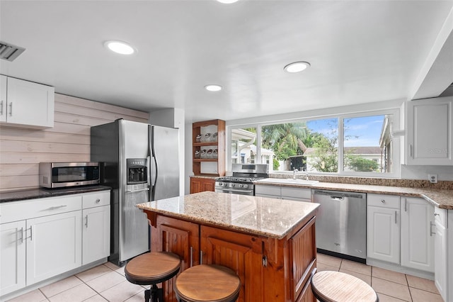 kitchen with light stone countertops, stainless steel appliances, white cabinetry, and a kitchen island