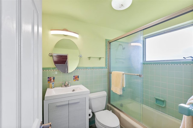 full bathroom with tile walls, vanity, toilet, and bath / shower combo with glass door