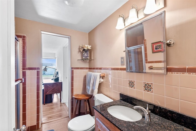 bathroom with tile walls, a shower with shower door, vanity, toilet, and hardwood / wood-style floors