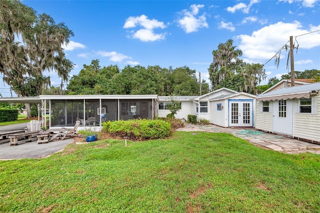 back of property with a lawn, a sunroom, french doors, and a patio area