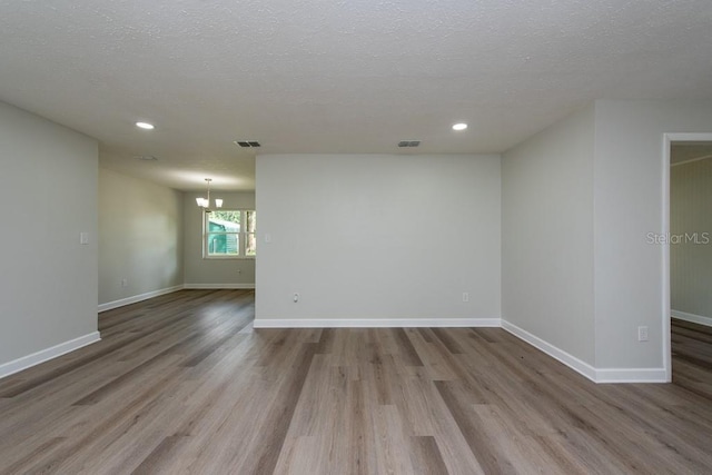 spare room with an inviting chandelier, a textured ceiling, and hardwood / wood-style flooring