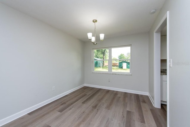 unfurnished room with a notable chandelier and light wood-type flooring