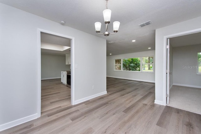 unfurnished dining area featuring a textured ceiling, light hardwood / wood-style flooring, and a notable chandelier