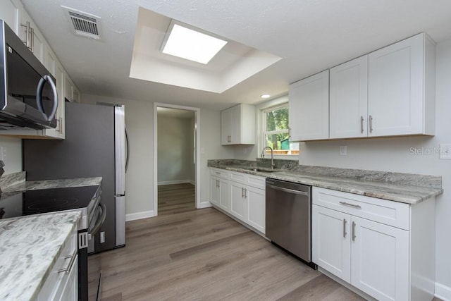 kitchen with white cabinets, light hardwood / wood-style flooring, stainless steel appliances, and a tray ceiling