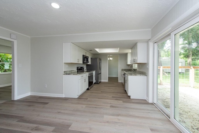 kitchen with appliances with stainless steel finishes, sink, dark stone countertops, white cabinets, and light hardwood / wood-style floors